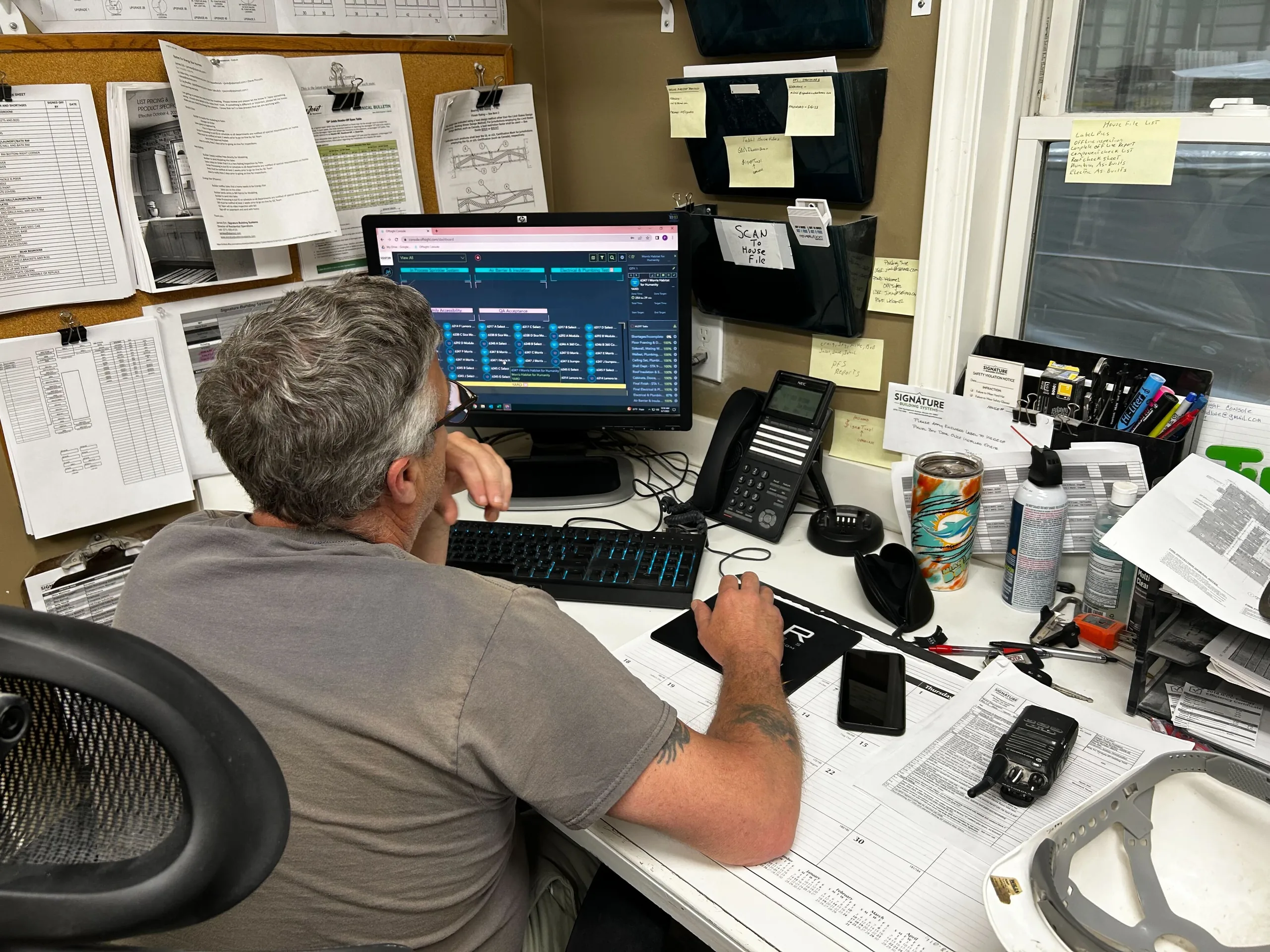 A plant office desk under a corkboard of printed spec sheets, with the Offsight console open