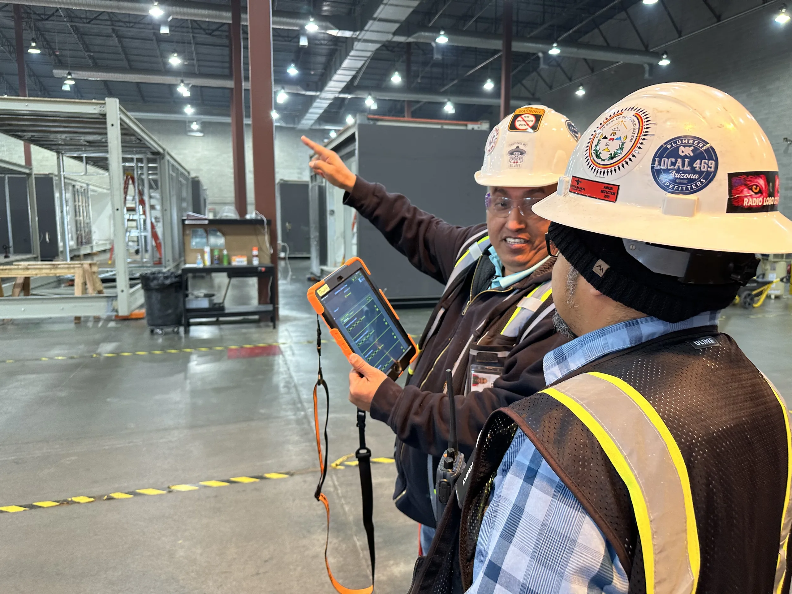 Two workers on the plant floor, one holding a rugged tablet
