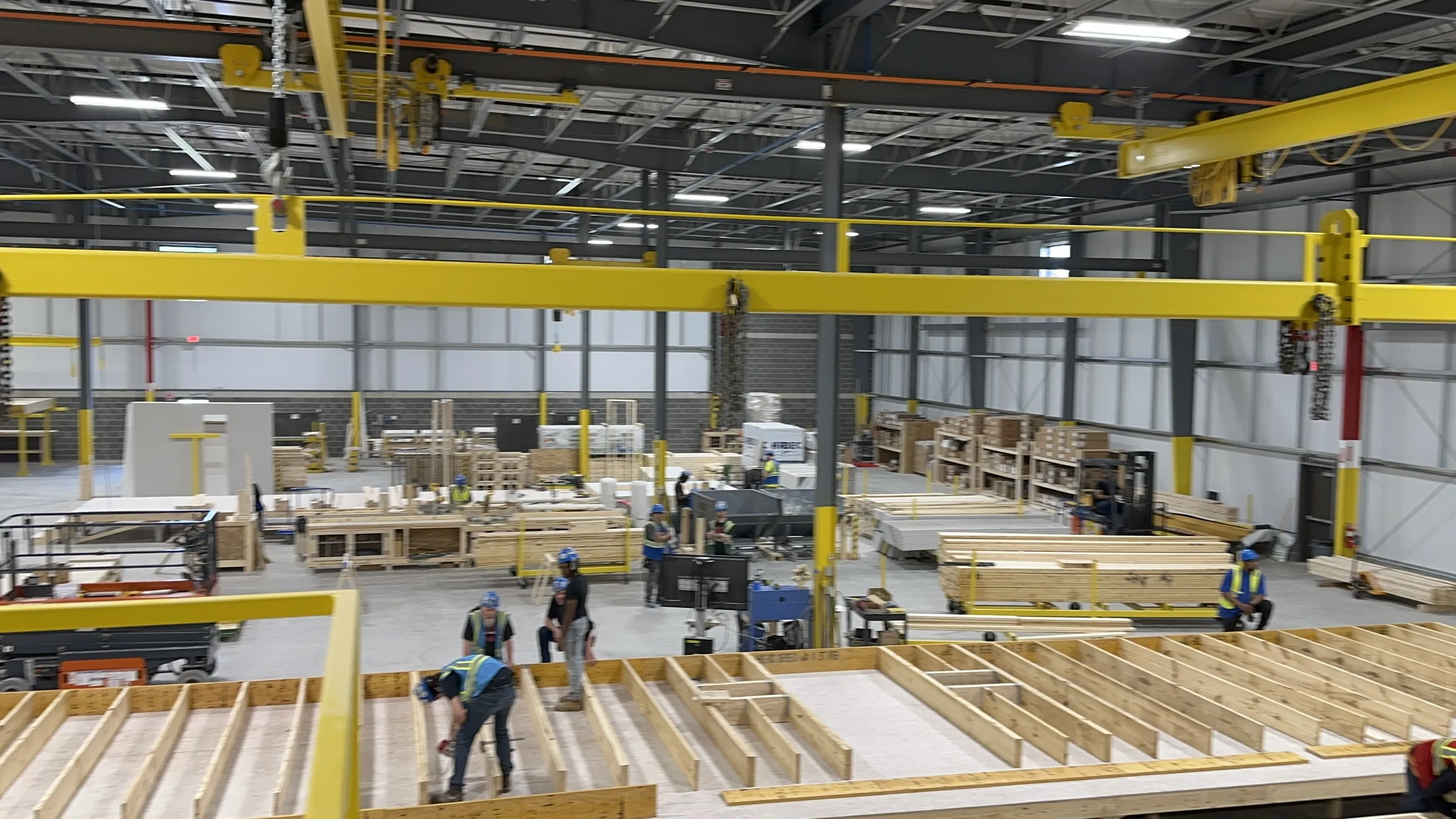 A prefab factory floor with wall panels being framed under an overhead crane