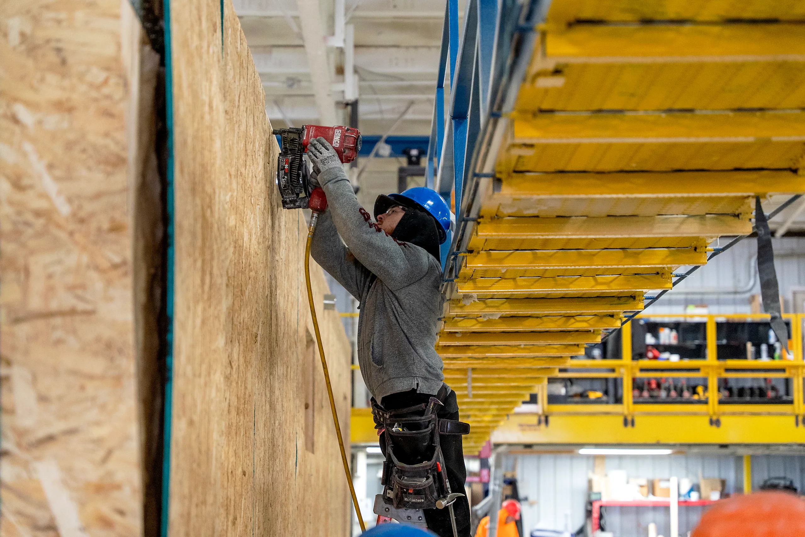 Two workers moving a sheathing panel on a prefabrication floor